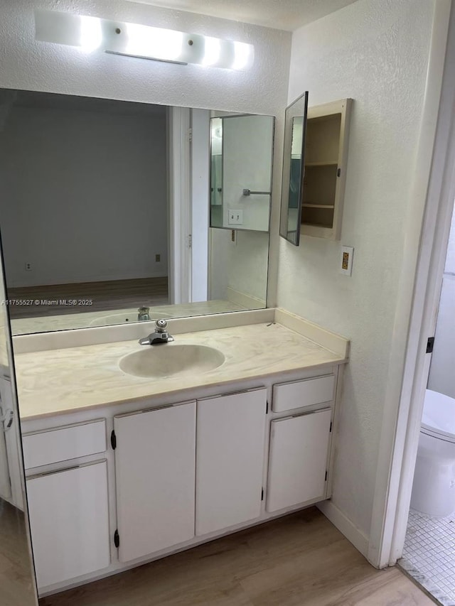 bathroom featuring toilet, a textured wall, wood finished floors, and vanity