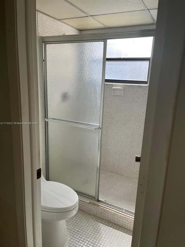 full bathroom with a paneled ceiling, a stall shower, toilet, and tile patterned floors