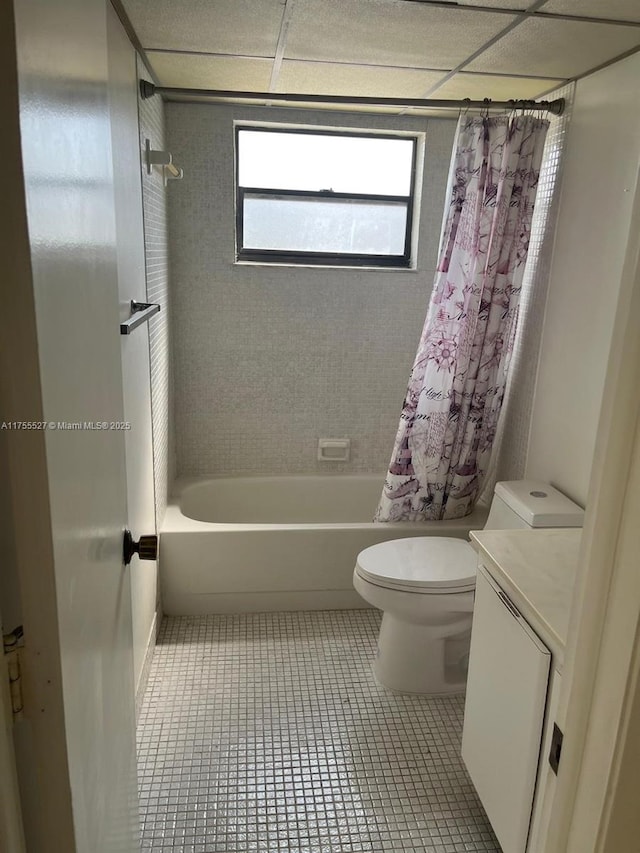 bathroom with a drop ceiling, toilet, shower / tub combo with curtain, tile patterned floors, and vanity