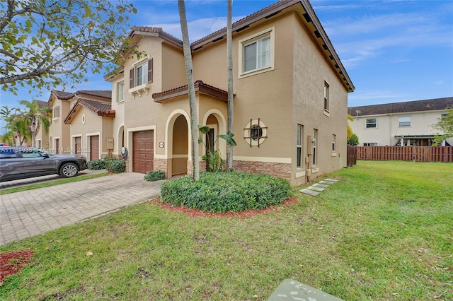 view of front facade with an attached garage, fence, decorative driveway, a front yard, and stucco siding