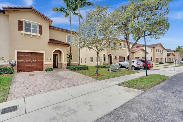 view of front of home featuring a garage, a residential view, a tiled roof, decorative driveway, and stucco siding