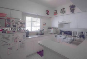 kitchen featuring light countertops, white cabinetry, a sink, a peninsula, and under cabinet range hood