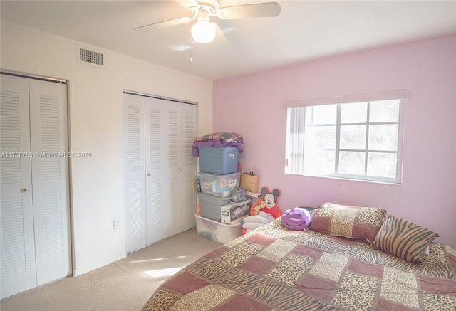 bedroom featuring carpet floors, visible vents, ceiling fan, and two closets