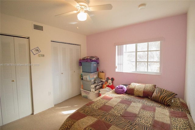 bedroom with two closets, ceiling fan, visible vents, and carpet flooring