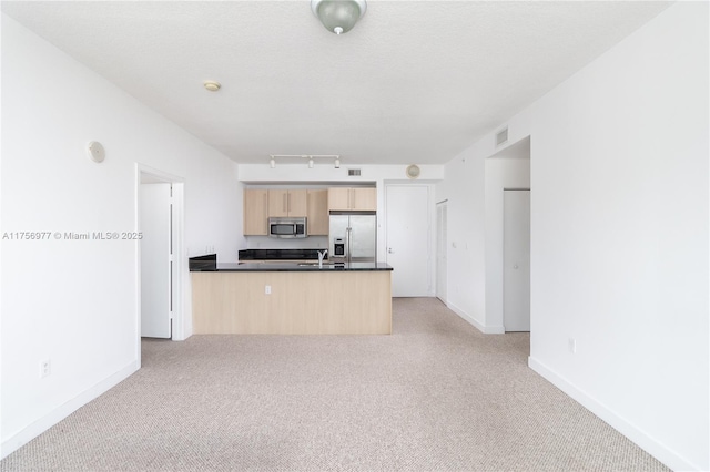 kitchen with light carpet, dark countertops, appliances with stainless steel finishes, a peninsula, and light brown cabinetry