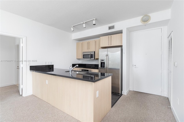 kitchen featuring light brown cabinets, stainless steel appliances, a peninsula, a sink, and carpet