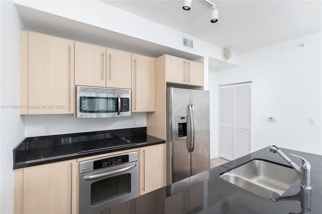 kitchen with visible vents, dark countertops, appliances with stainless steel finishes, light brown cabinets, and a sink