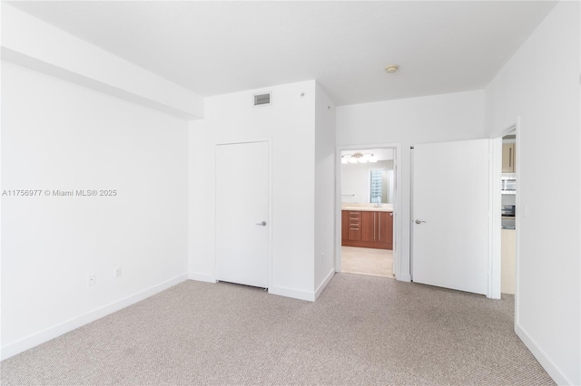 unfurnished bedroom with ensuite bathroom, carpet floors, visible vents, and baseboards