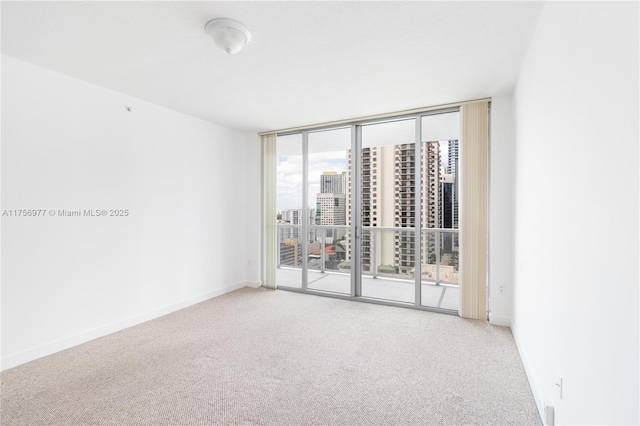 spare room featuring a wall of windows, carpet, baseboards, and a view of city