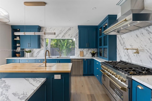 kitchen with blue cabinets, wall chimney range hood, stainless steel appliances, and light wood finished floors