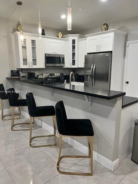 kitchen featuring dark countertops, white cabinets, stainless steel appliances, and a kitchen breakfast bar