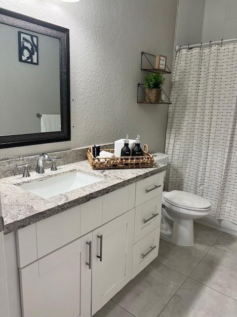 full bath featuring a textured wall, toilet, tile patterned floors, vanity, and a shower with curtain