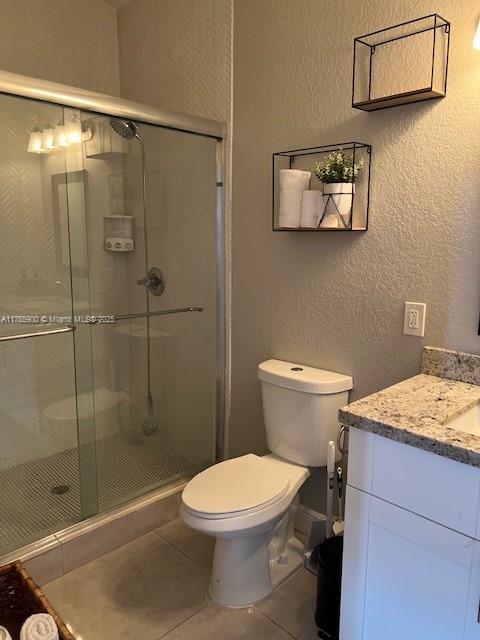 full bathroom featuring a textured wall, a stall shower, tile patterned flooring, and toilet