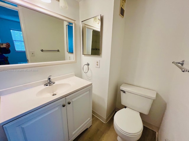 half bathroom featuring visible vents, baseboards, toilet, wood finished floors, and vanity