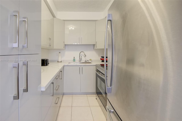 kitchen with appliances with stainless steel finishes, white cabinetry, a sink, a textured ceiling, and tile patterned floors