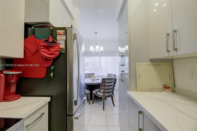 kitchen featuring white cabinets, light stone countertops, a textured ceiling, a notable chandelier, and light tile patterned flooring