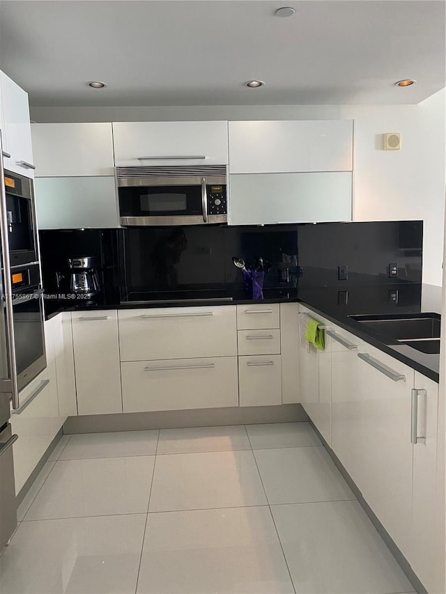 kitchen with white cabinets, appliances with stainless steel finishes, dark countertops, tasteful backsplash, and modern cabinets