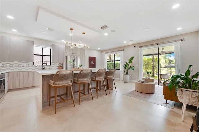 kitchen featuring tasteful backsplash, light countertops, freestanding refrigerator, modern cabinets, and a kitchen bar