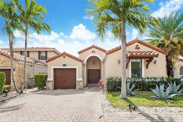 mediterranean / spanish house with decorative driveway, a tiled roof, an attached garage, and stucco siding