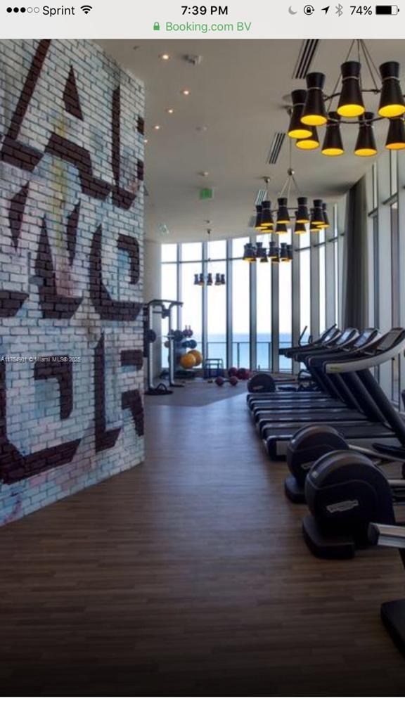 workout area with brick wall, a wall of windows, wood finished floors, and an inviting chandelier