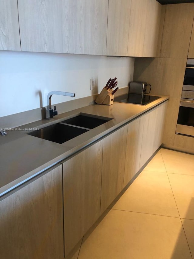 kitchen with light tile patterned floors, black electric stovetop, a sink, light countertops, and modern cabinets