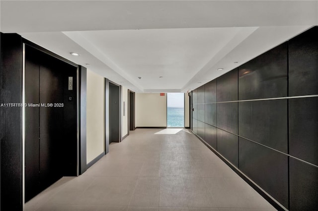 corridor featuring baseboards, elevator, and floor to ceiling windows