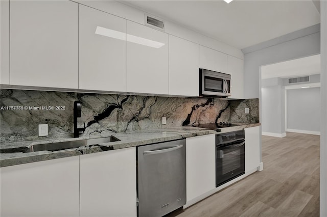 kitchen featuring visible vents, light stone counters, black appliances, white cabinetry, and a sink