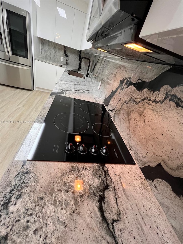 kitchen featuring light stone counters, light wood-style flooring, black electric cooktop, white cabinets, and modern cabinets