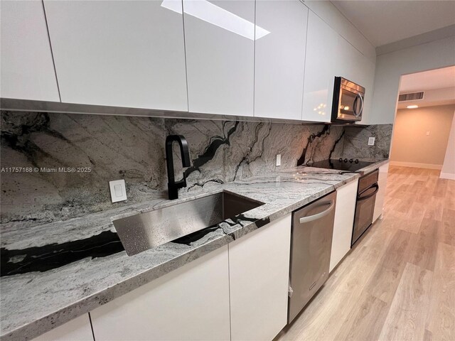 kitchen featuring visible vents, white cabinetry, a sink, modern cabinets, and black appliances