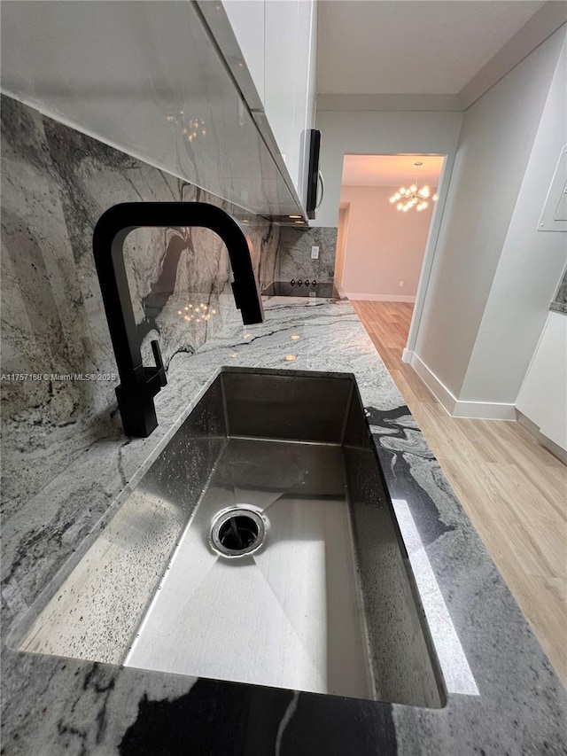 details featuring tasteful backsplash, baseboards, wood finished floors, a sink, and a notable chandelier