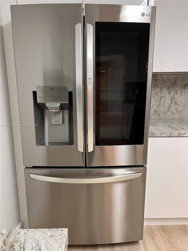 room details featuring light wood finished floors, stainless steel refrigerator with ice dispenser, light stone counters, and white cabinets