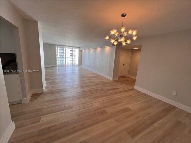 spare room with light wood-style flooring, baseboards, and a notable chandelier