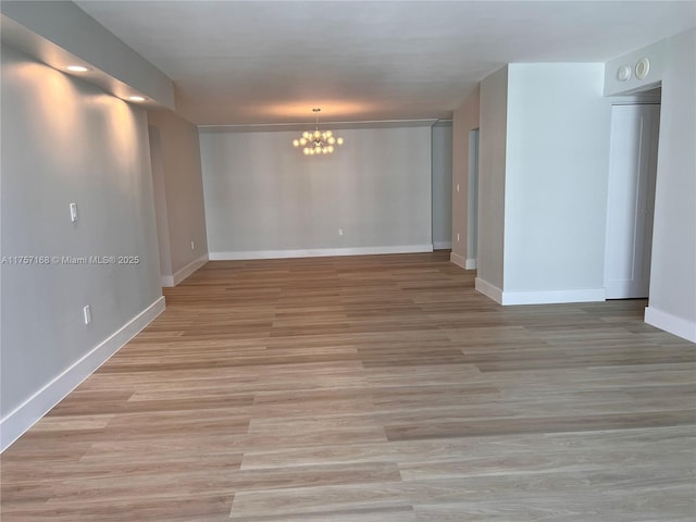 spare room with baseboards, light wood-type flooring, and an inviting chandelier