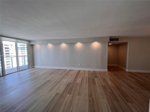 empty room featuring expansive windows, baseboards, and wood finished floors