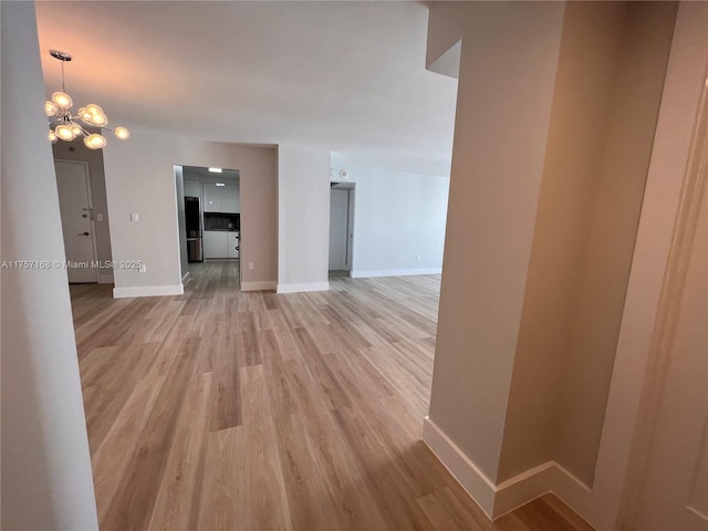 unfurnished living room with a chandelier, light wood-style flooring, and baseboards