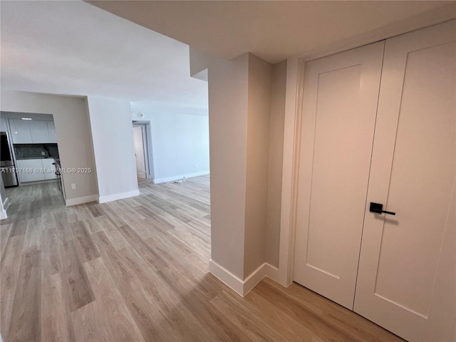 corridor featuring baseboards and light wood finished floors