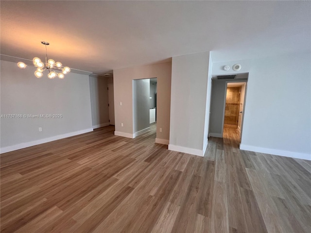 empty room with a notable chandelier, wood finished floors, and baseboards