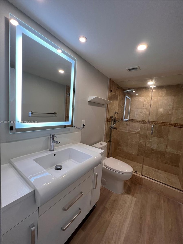 bathroom with toilet, wood finished floors, vanity, visible vents, and a shower stall