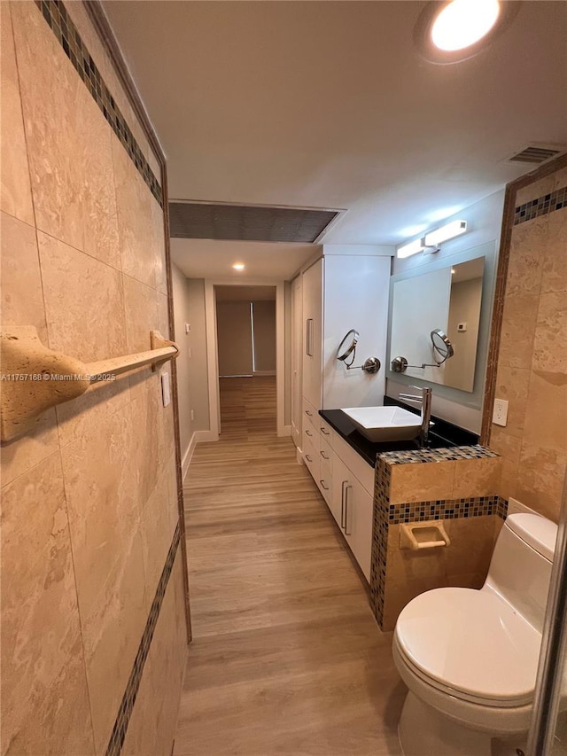 bathroom with toilet, wood finished floors, vanity, visible vents, and tile walls