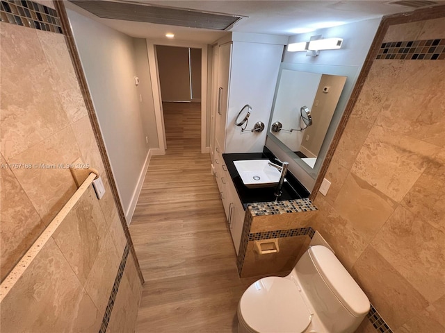 bathroom with vanity, wood finished floors, toilet, and tile walls