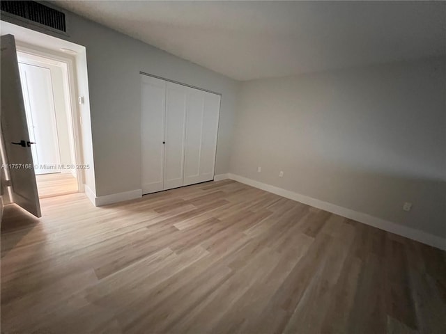 unfurnished bedroom featuring light wood-style floors, baseboards, visible vents, and a closet