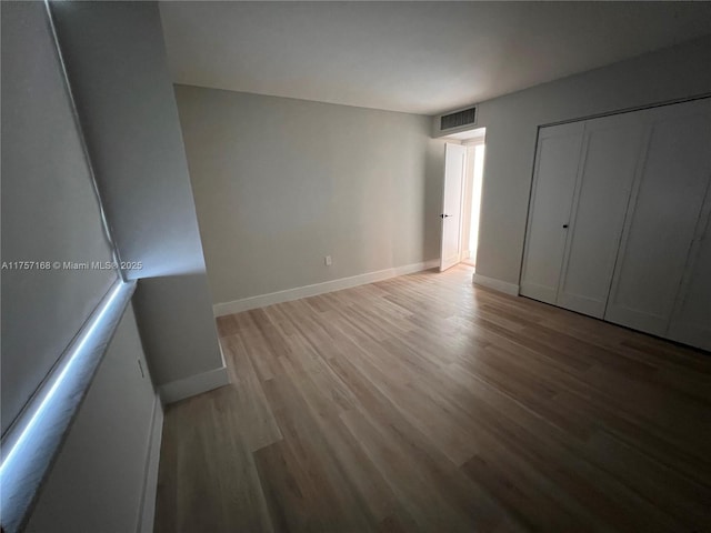 unfurnished bedroom featuring baseboards, a closet, visible vents, and wood finished floors