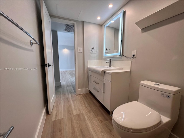 half bath with visible vents, baseboards, toilet, wood finished floors, and vanity