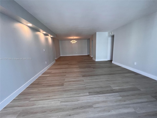 empty room with wood finished floors, baseboards, and an inviting chandelier