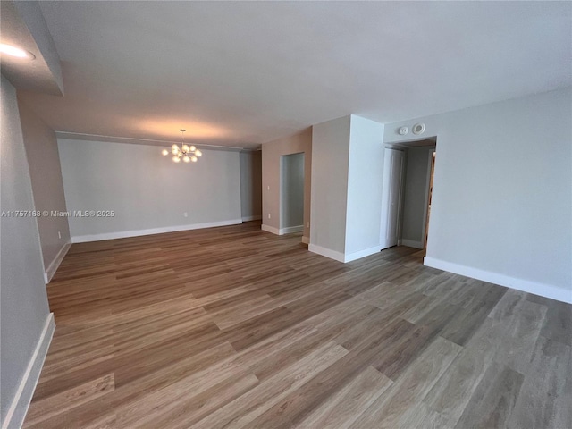 unfurnished room featuring baseboards, a notable chandelier, and wood finished floors