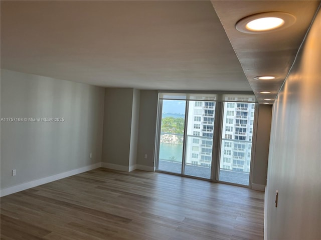 unfurnished room featuring floor to ceiling windows, wood finished floors, and baseboards