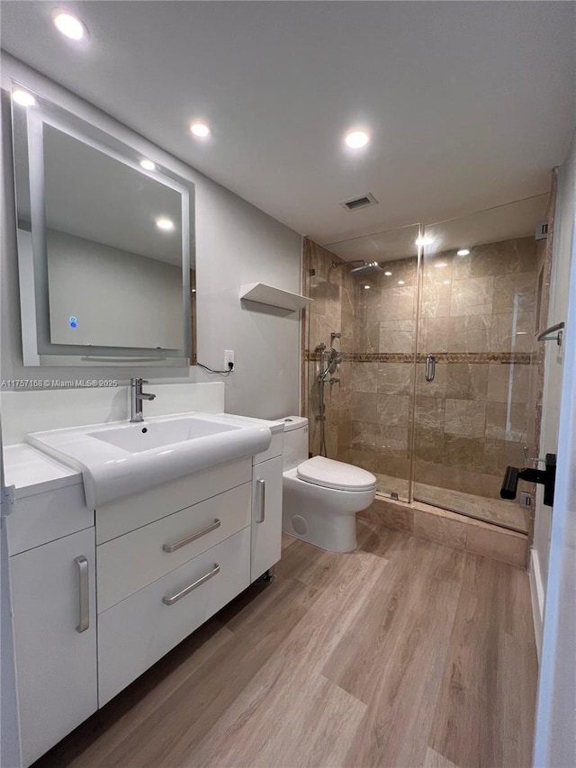 bathroom featuring toilet, wood finished floors, visible vents, vanity, and a stall shower