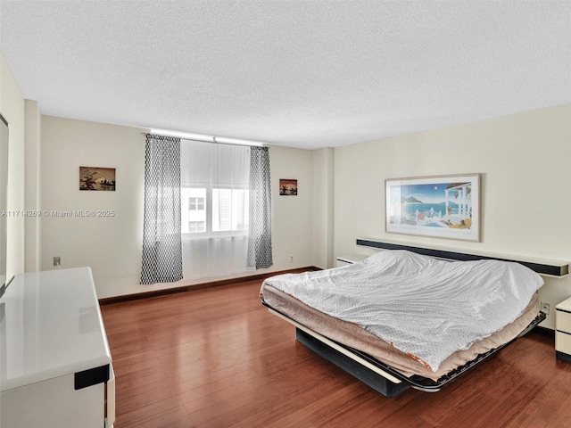 bedroom with a textured ceiling, baseboards, and wood finished floors