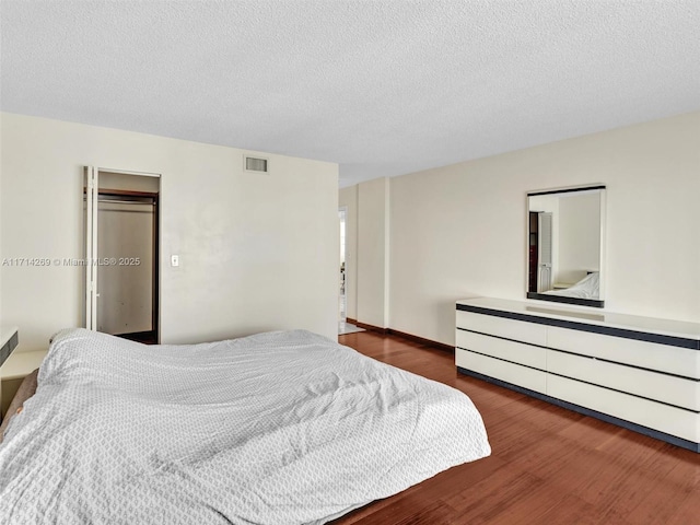 bedroom with a textured ceiling, wood finished floors, and visible vents