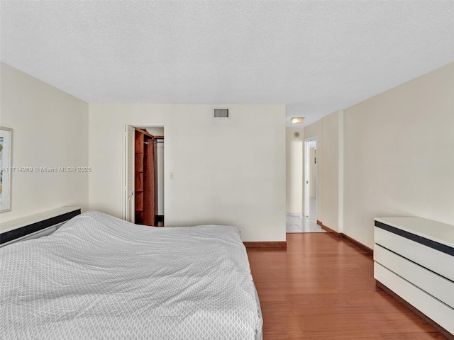 bedroom with a textured ceiling, wood finished floors, visible vents, and baseboards